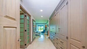 Un pasillo con puertas y armarios de madera, que conduce a una habitación con cama y vista a palmeras.