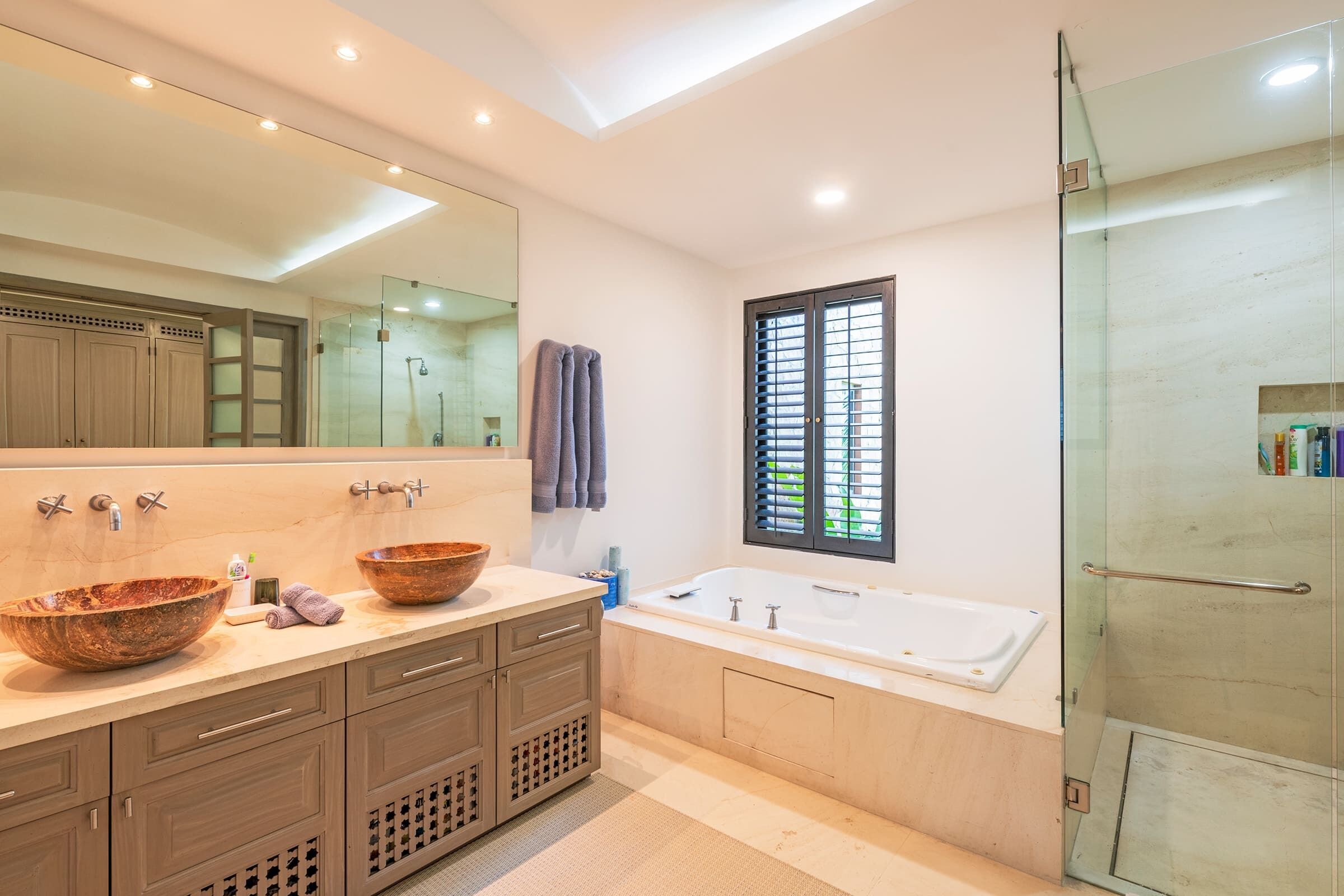 A modern bathroom with a large mirror, two sinks, a bathtub, and a glass-enclosed shower.