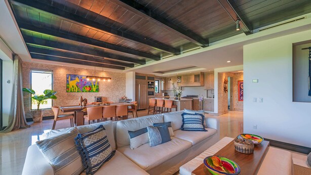 Una sala moderna con sofá modular, comedor, cocina y un amplio ventanal con vistas.