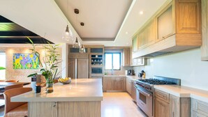 Una cocina moderna con armarios de madera, una isla central, iluminación colgante y un amplio ventanal.