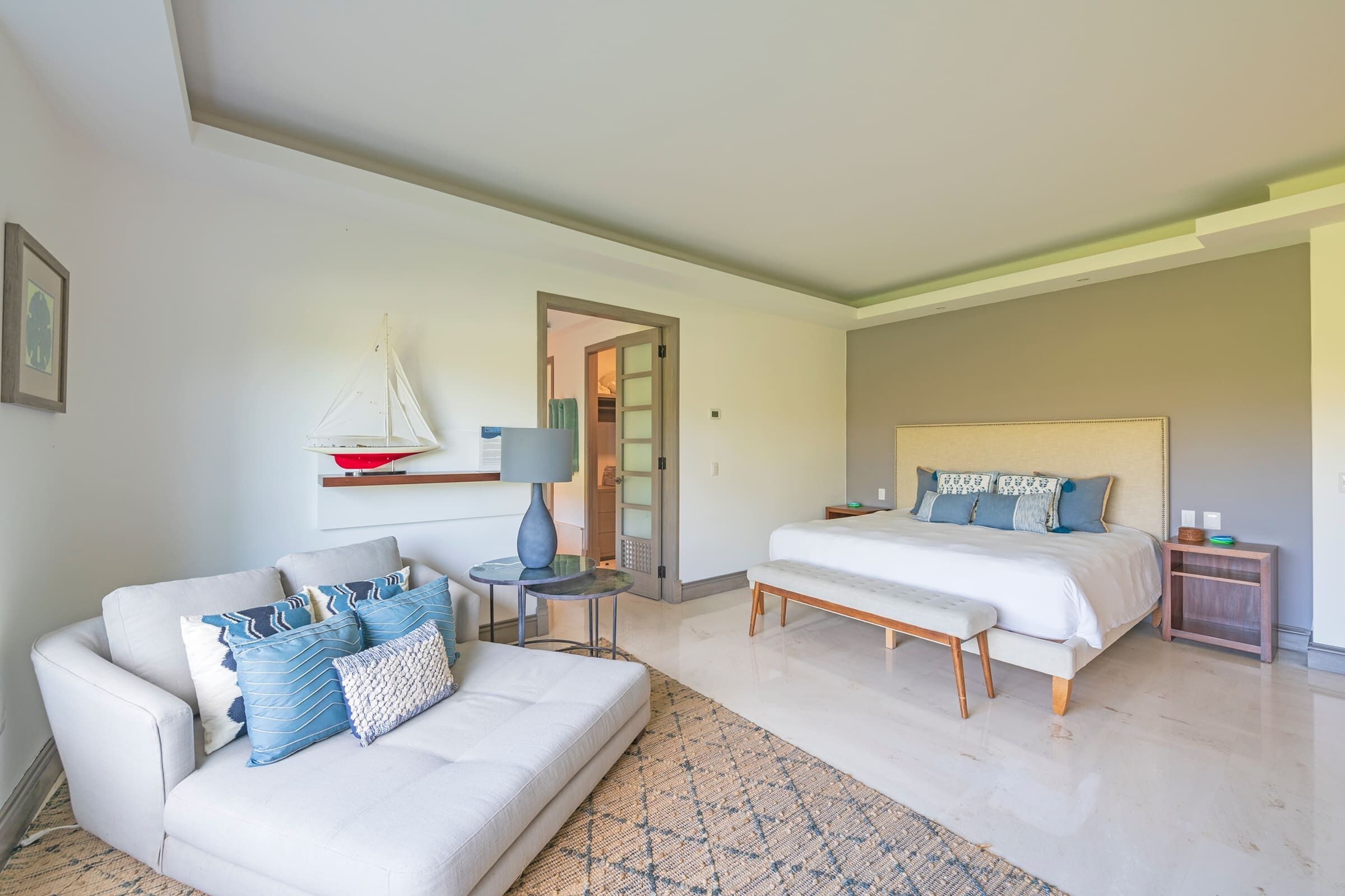 Una habitación de hotel moderna con un sofá, dos camas, una mesita y un velero decorativo.