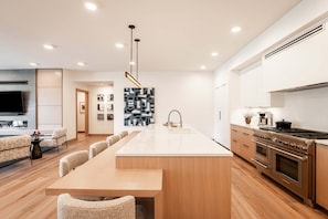 Una cocina moderna con una isla central, horno empotrado y una zona de comedor con una mesa larga y sillas.