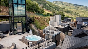 Un edificio moderno con una torre de vidrio, asientos al aire libre, un jacuzzi y vistas a colinas verdes.