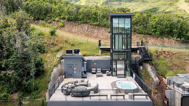 Un edificio moderno con piscina, mobiliario exterior y vista a un paisaje montañoso.