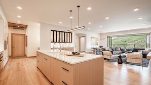 Una cocina moderna con una isla grande, armarios de madera y un comedor con sofás y un ventanal amplio.