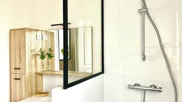 Een moderne badkamer met een houten wastafelmeubel, een spiegel, een douche met een handdouche en witte betegelde wanden.
