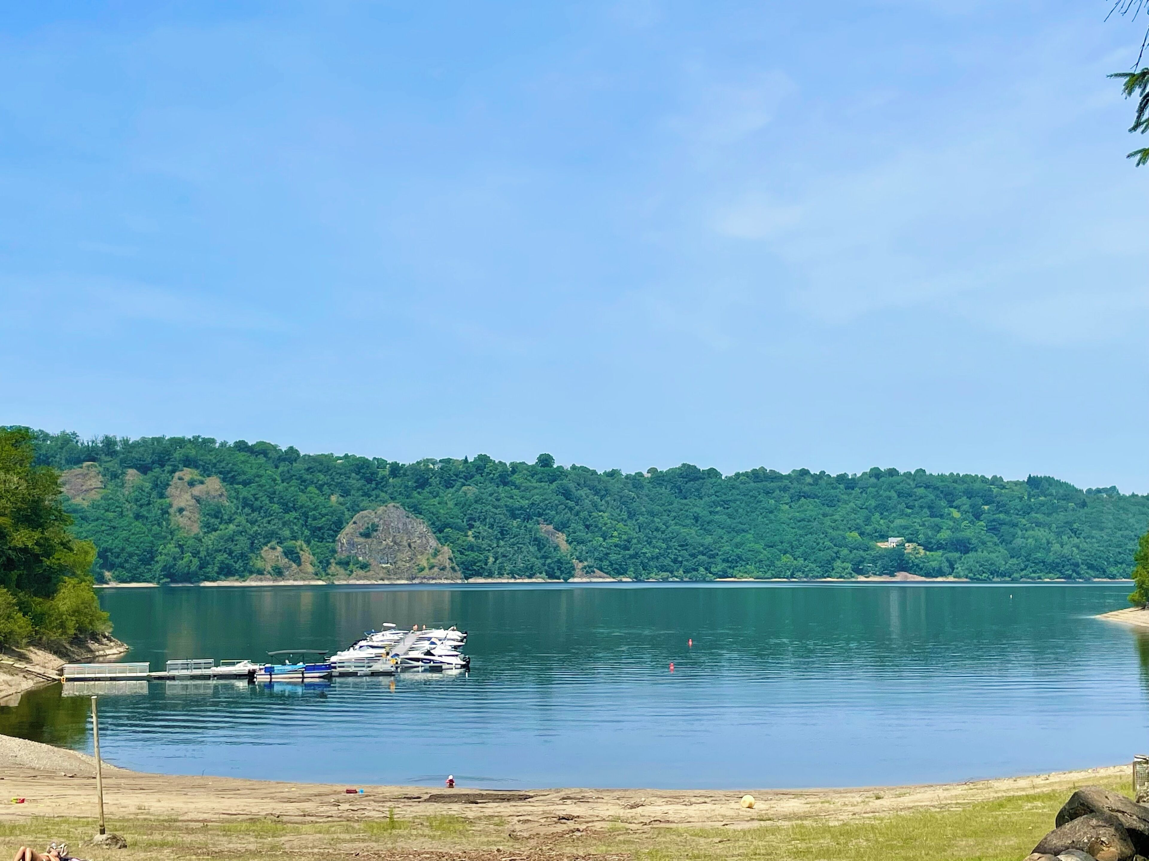 A lake with boats docked at a pier, surrounded by dense forest.