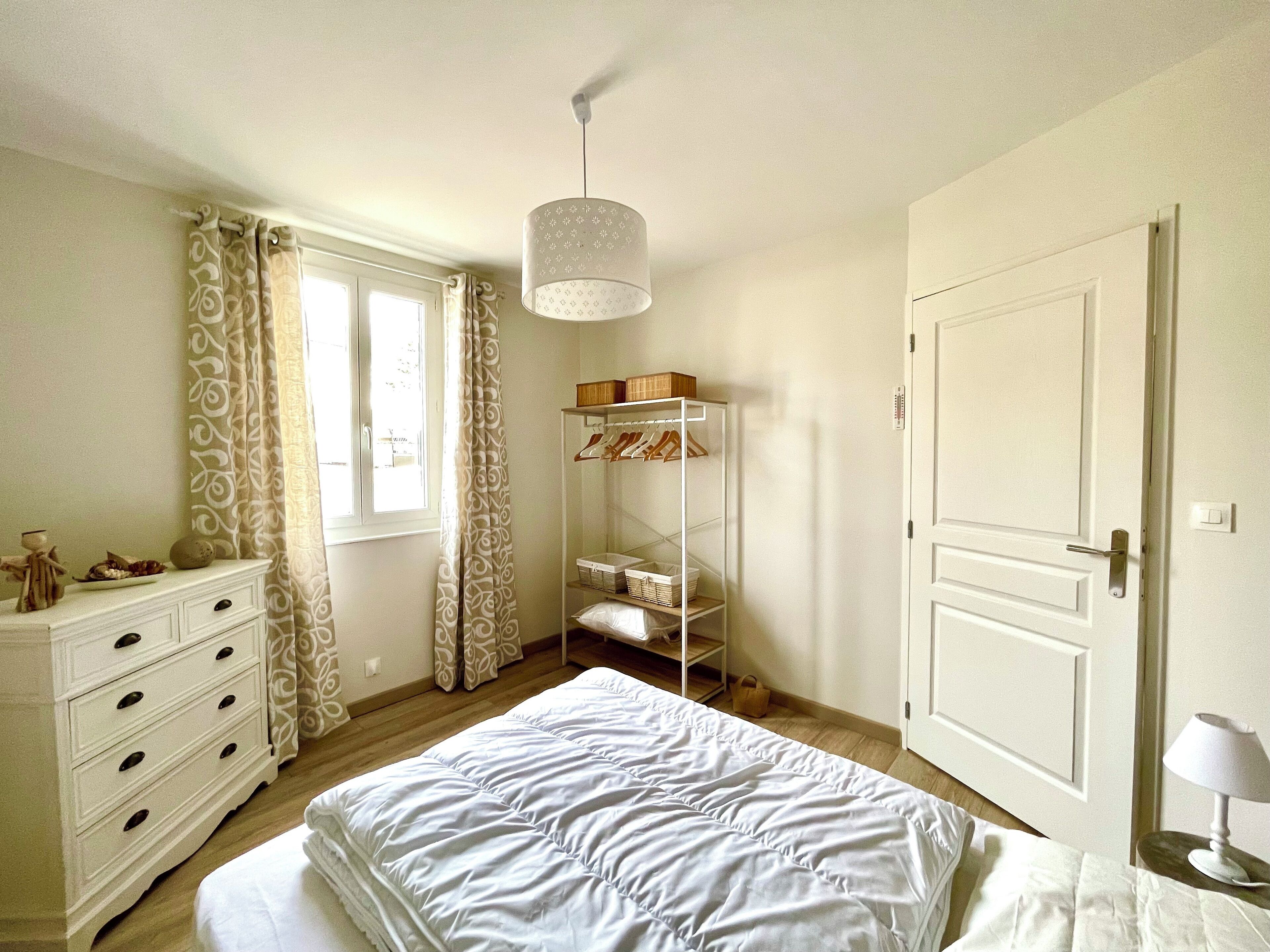 Un dormitorio con cama, cómoda, armario y lámpara colgante.
