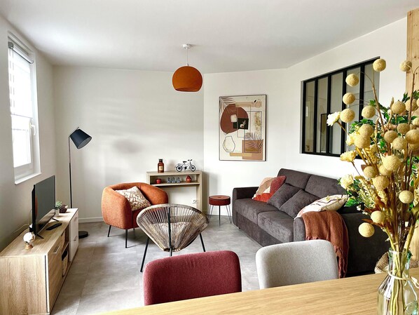 Een moderne woonkamer met een bank, stoelen, een salontafel en een televisie op een houten kast.