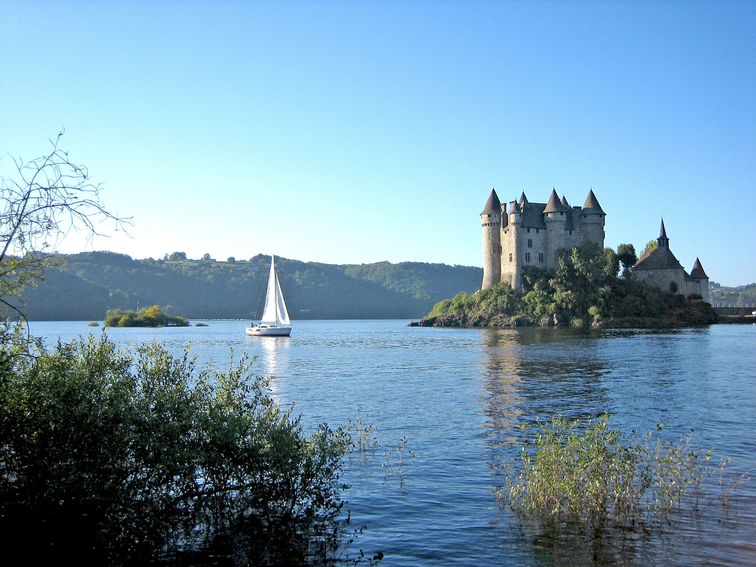 Een kasteel op een eiland, met een zeilboot in het water.