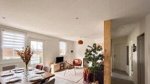 Een moderne woonkamer met een eethoek, een televisie en een groot raam.