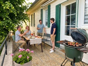 Een terras met een eettafel, een barbecue met eten en een bloempot.