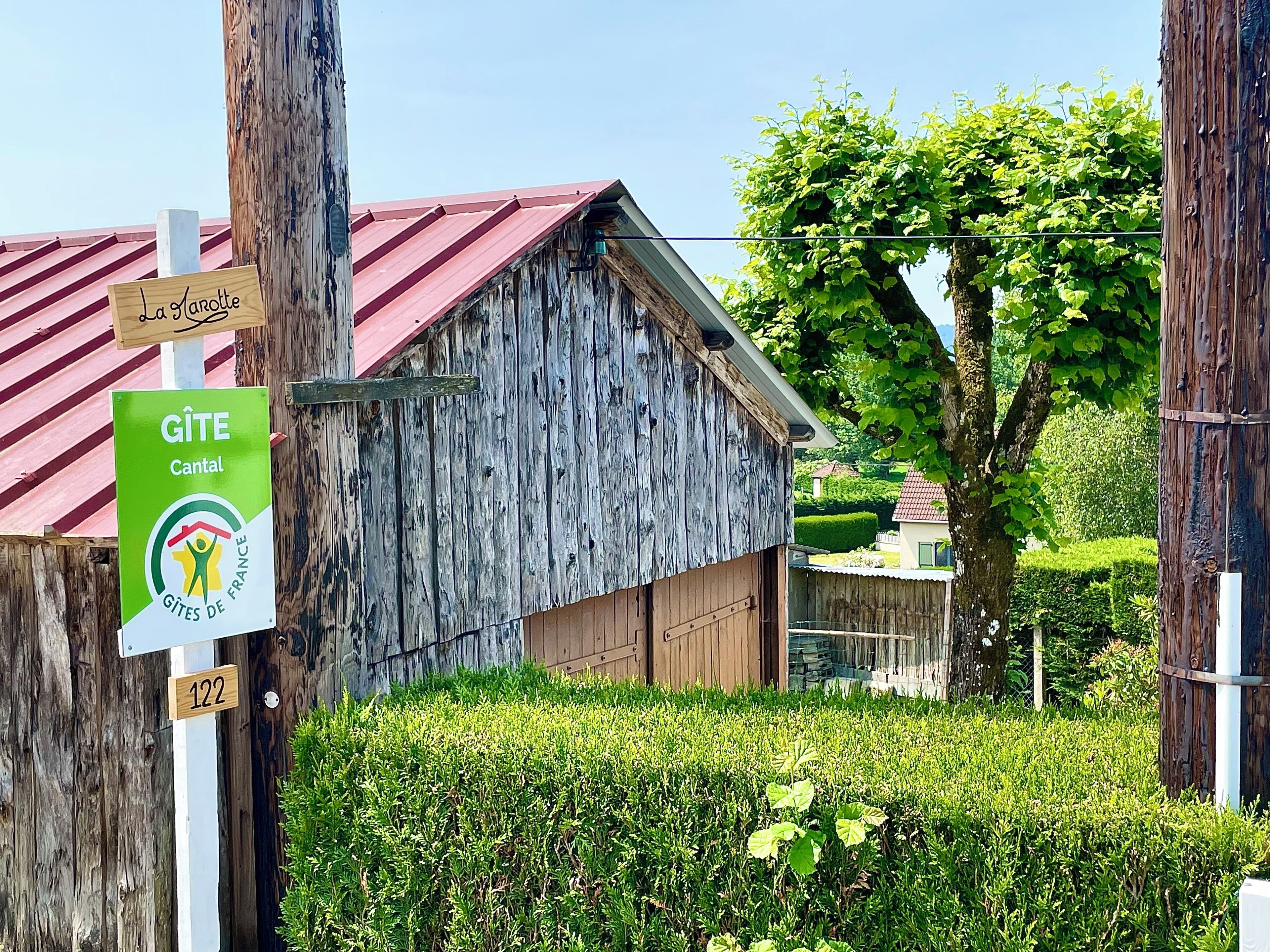 Un bâtiment rustique en bois, avec un toit rouge, une enseigne indiquant qu’il s’agit d’un gîte situé dans le Cantal, et une plaque portant le numéro 122.