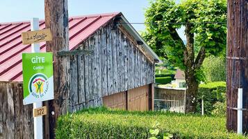 Un bâtiment rustique en bois, avec un toit rouge, une enseigne indiquant qu’il s’agit d’un gîte situé dans le Cantal, et une plaque portant le numéro 122.