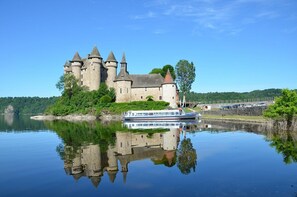 Een kasteel met meerdere torens, een boot afgemeerd ervoor, en een rustig meer dat de structuur weerspiegelt.