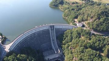 A large dam with a road passing over it, surrounded by lush greenery and a lake.