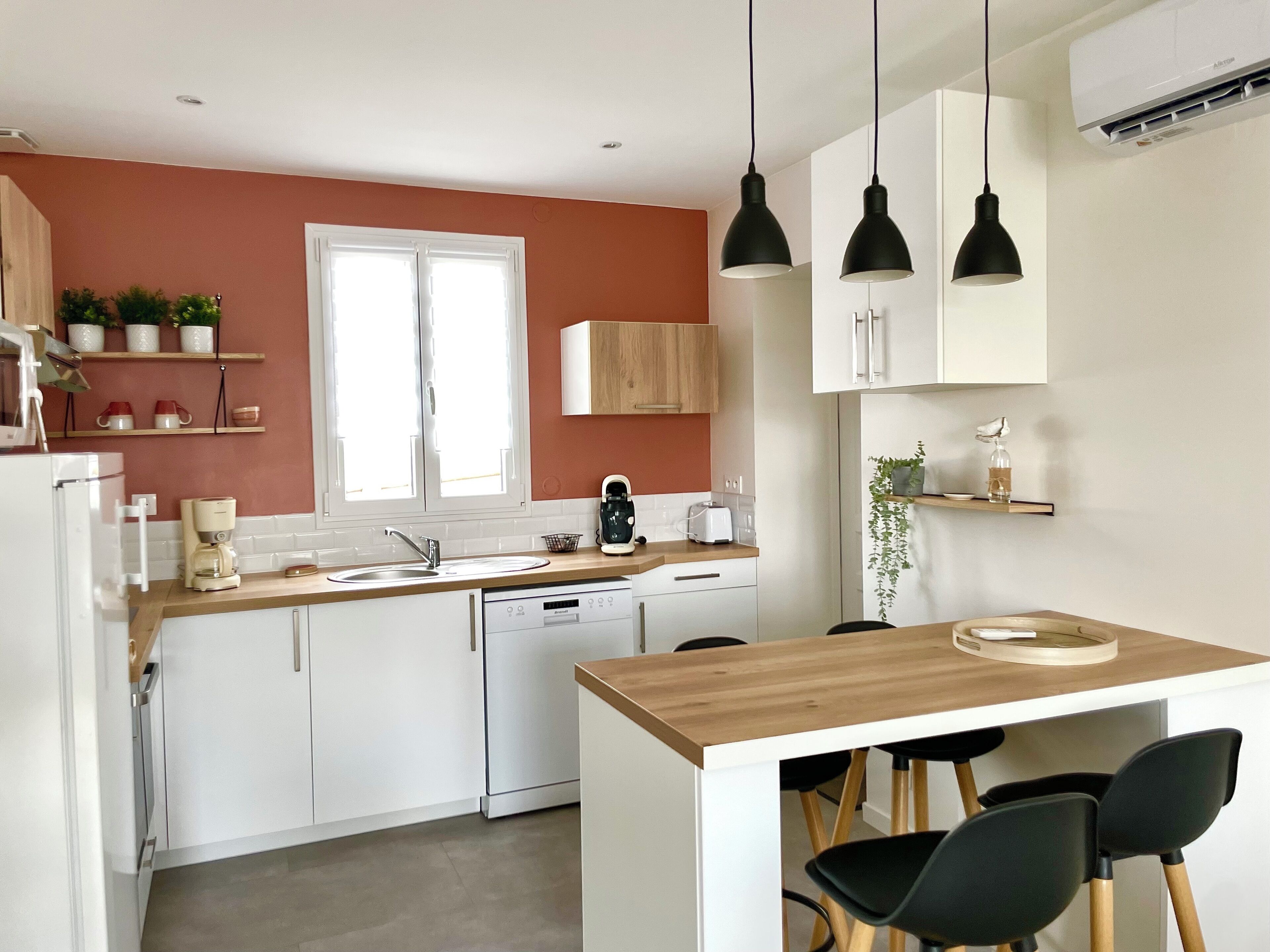 Eine moderne Küche mit weißen Schränken, einer Holz Arbeitsplatte, einem eingebauten Geschirrspüler und einer kleinen Essecke mit zwei schwarzen Stühlen.