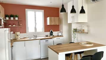 Eine moderne Küche mit weißen Schränken, einer Holz Arbeitsplatte, einem eingebauten Geschirrspüler und einer kleinen Essecke mit zwei schwarzen Stühlen.