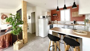 Een moderne keuken met witte kasten, een centraal kookeiland, zwarte barkrukken en hanglampen.