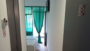 A narrow hallway leading to a bedroom with a bed, a television mounted on the wall, and a door with a no-smoking sign. - H. Central Funchal 17 (Funchal)