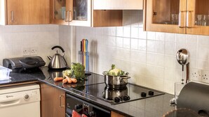 A kitchen with wooden cabinets, a gas stove, a kettle, and a dish rack. - Protaras Apollon Seaside Villa (Paralimni)