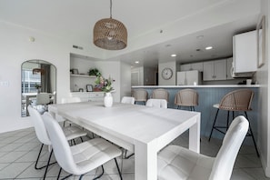 Une cuisine moderne avec des meubles blancs, un coin repas doté d’une table et de chaises blanches, et des chaises en osier à l’arrière-plan.