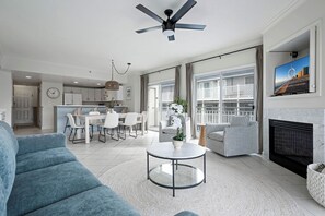 Una sala de estar moderna con un sofá azul, una mesa de centro redonda, una chimenea y un televisor montado en la pared.