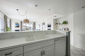 Une cuisine moderne avec des meubles blancs, un évier à deux bacs, un lave-vaisselle et un luminaire suspendu.