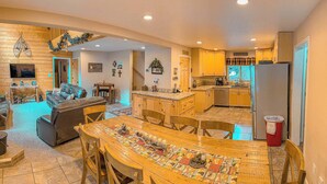 Una sala de estar acogedora con chimenea, un comedor con mantel estampado y una cocina con armarios de madera y refrigerador.