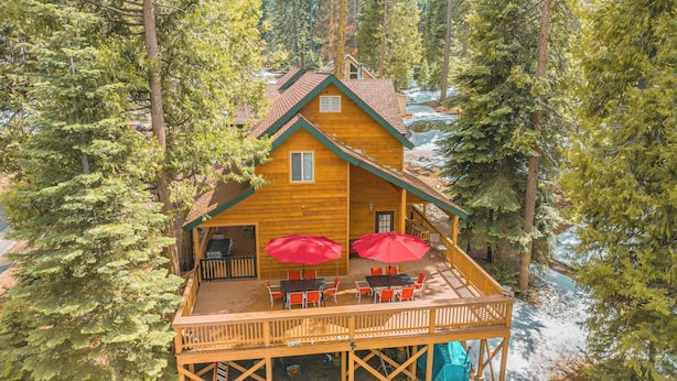 Una cabaña de madera con terraza, sombrillas rojas y vista a un área boscosa.