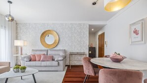 Una sala moderna con un sofá gris, un espejo redondo, una mesa de comedor con sillas rosadas y una pequeña mesita de noche con una lámpara.