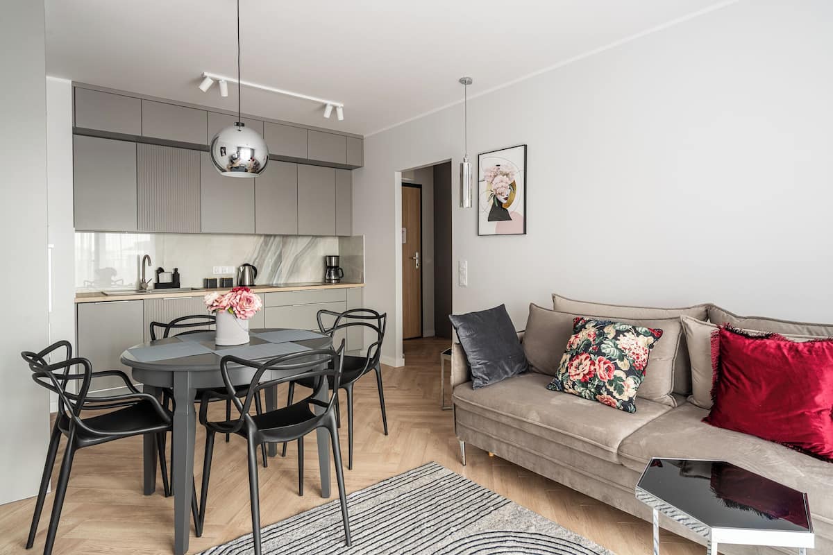 A modern living space with a dining area, kitchen, and a sofa with decorative pillows.
