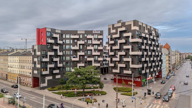 A modern building with a unique zigzag facade, a red section on the left, and a sign for "NOVA MANUFATURA" at the base. - RentPlanet - Nowa Manufaktura (Wroclaw)