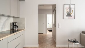 A modern kitchen with a coffee maker, a framed artwork, and a small table with a book. - RentPlanet - Nowa Manufaktura (Wroclaw)