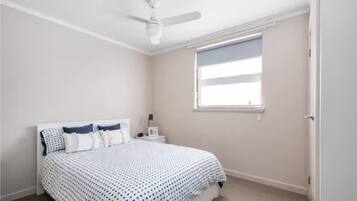 A bedroom with a bed, a nightstand, a ceiling fan, and a window.