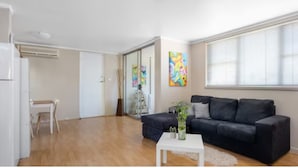 En moderne stue med en mørk sofa, et hvidt sofabord og et stort vindue med persienner.