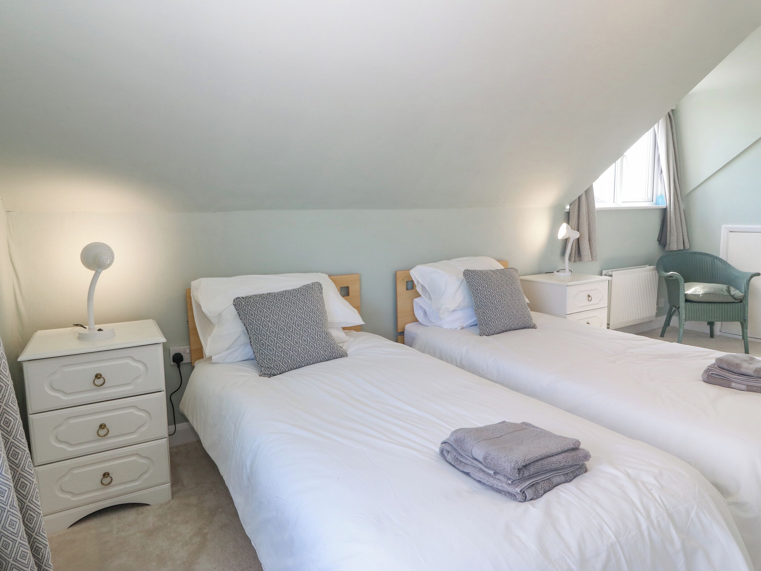 A twin room with two beds, a bedside table, a chair, a desk, and a lamp.