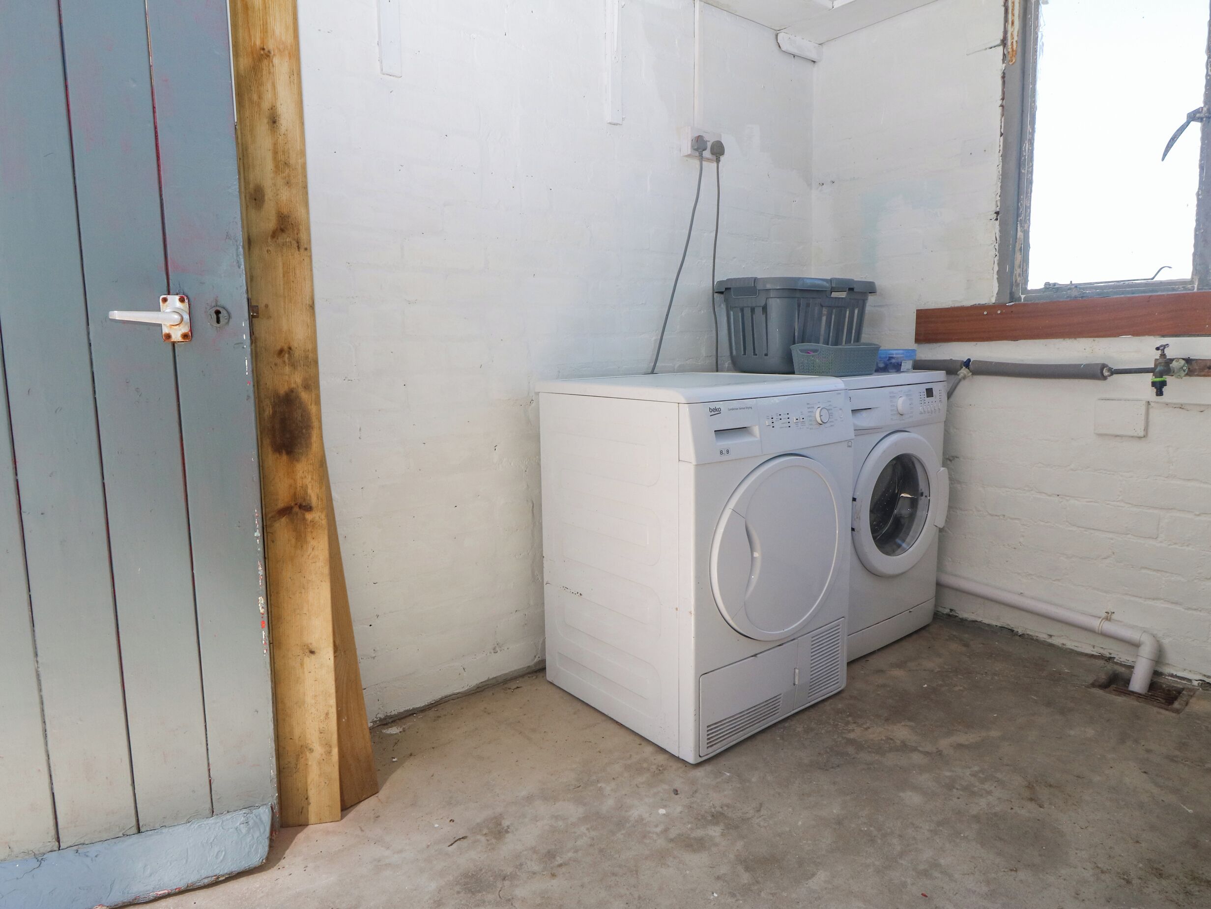 A laundry area with a washing machine and a dryer, a wooden door, and a window.