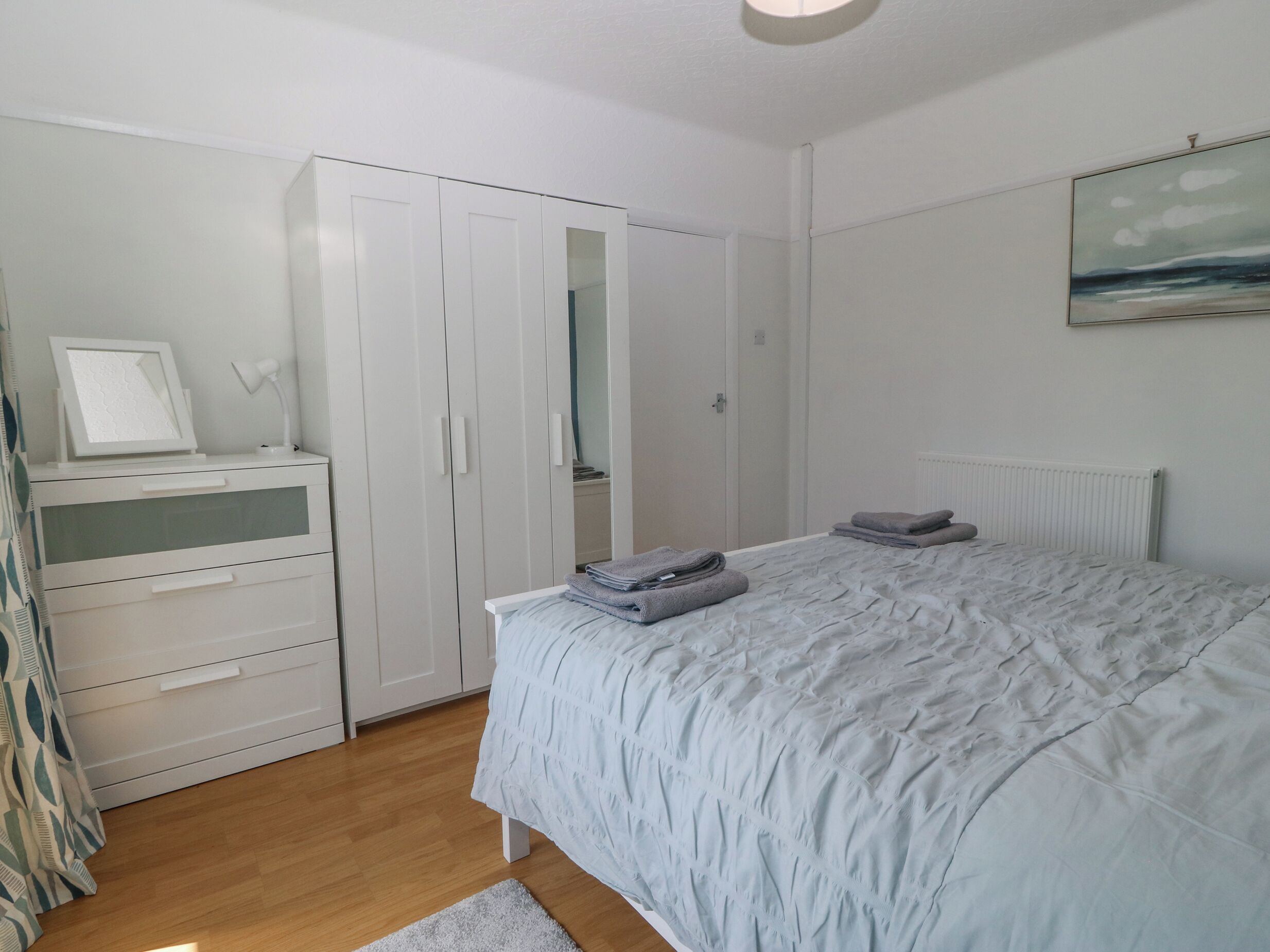 A bedroom with a bed, a wardrobe, a mirror, and a painting on the wall.