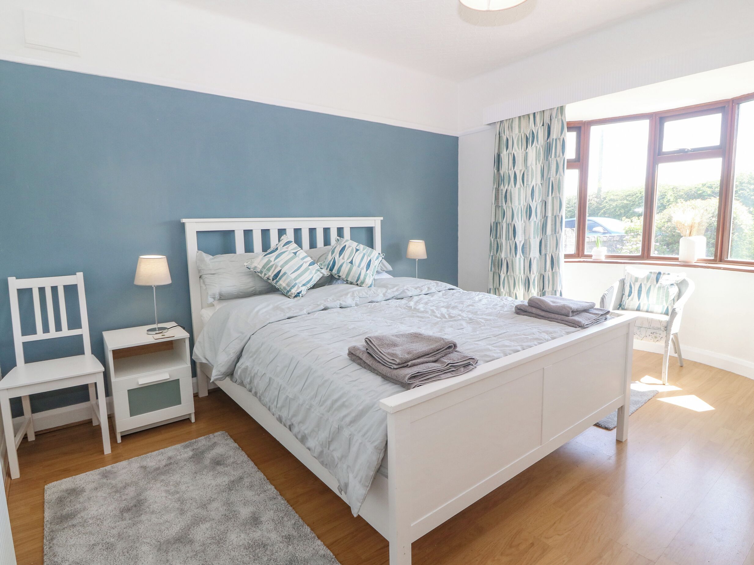 Une chambre à coucher avec un lit, des tables de chevet, une chaise et une fenêtre avec des rideaux.