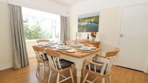 A dining room with a wooden table set for four, surrounded by four chairs with cushions. A painting of a bridge over water is on the wall. - Awelfryn (Holyhead)