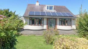 A house with solar panels on the roof, a small window, and a garden. - Awelfryn (Holyhead)