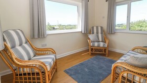 A room with two wicker chairs with striped cushions, a blue rug, and large windows with curtains. - Awelfryn (Holyhead)