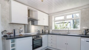A modern kitchen with white cabinetry, a built-in oven, a stovetop, and a window providing natural light. - Awelfryn (Holyhead)