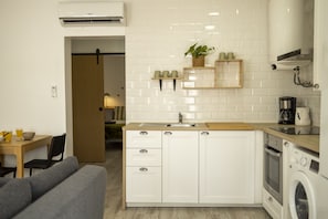 A compact kitchen with white cabinets, a built-in oven, a washing machine, and a coffee maker.