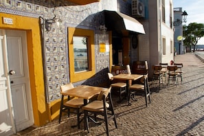A café with outdoor seating, a tiled wall, and a view of the water.