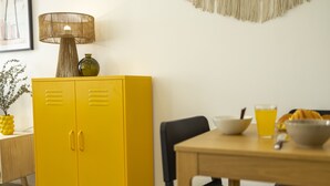 Un armario amarillo con dos puertas, una lámpara, un florero y una mesa con un cuenco y un vaso.