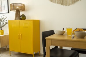 A yellow cabinet with two doors, a lamp, a vase, and a table with a bowl and a glass.