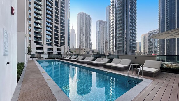Un espace piscine aménagé sur le toit, avec des chaises longues et une vue dégagée sur les immeubles environnants.