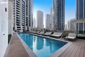 A rooftop pool area with lounge chairs and a clear view of surrounding high-rise buildings. - bnbme | Act One Act Two | 1 BDR (Dubai)